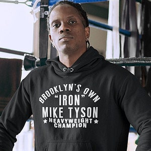 May include: Black hooded sweatshirt with white text that reads "Brooklyn's Own "Iron" Mike Tyson Heavyweight Champion" with a star on either side of the word "Heavyweight".