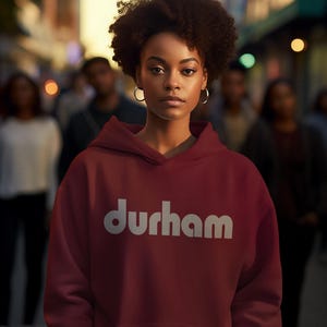 Pu&ograve; includere: Una felpa con cappuccio color bordeaux con un logo bianco "durham" sul davanti. La felpa ha un cappuccio con coulisse e una tasca a marsupio.