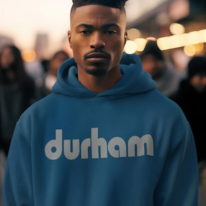 Pu&ograve; includere: Una felpa con cappuccio blu con la scritta "durham" stampata in bianco sul davanti.