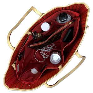 May include: A red and beige tote bag with multiple pockets and compartments. The bag is open and filled with various items, including a phone, keys, a water bottle, and a small pouch.