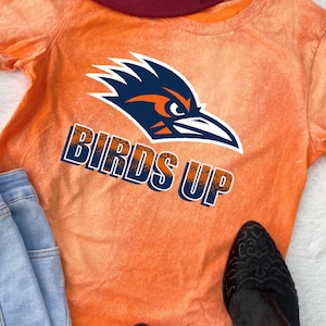 May include: Orange tie-dye t-shirt with a blue and orange bird graphic and the text "BIRDS UP" in a distressed font.