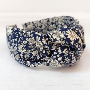 May include: A navy blue headband with a white floral pattern. The headband is knotted on top and is made of fabric.
