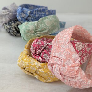 May include: A set of six knotted headbands in various floral patterns. The headbands are made of fabric and have a soft, comfortable feel. The colors include light blue, green, pink, red, yellow, and gray.