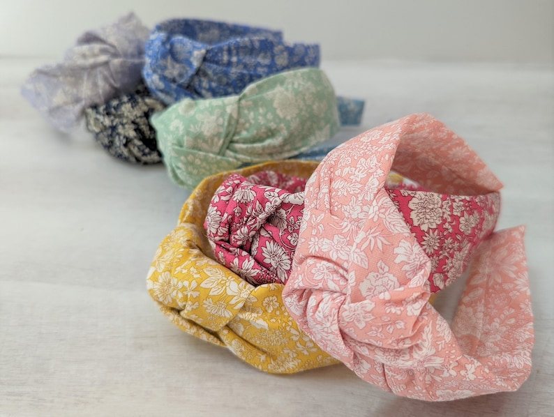 May include: A set of six knotted headbands in various floral patterns. The headbands are made of fabric and have a soft, comfortable feel. The colors include light blue, green, pink, red, yellow, and gray.