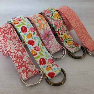 May include: Five colorful fabric straps with D-rings. The straps feature floral and patterned designs in shades of red, pink, orange, yellow, and white. The D-rings are silver and bronze. These straps are likely for bags or accessories.