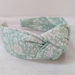 May include: A green headband with a white floral pattern. The headband is knotted in the front.