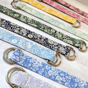Puede incluir: Un conjunto de siete cinturones de tela coloridos con un patr&oacute;n floral. Cada cintur&oacute;n tiene una hebilla de doble D de plata.