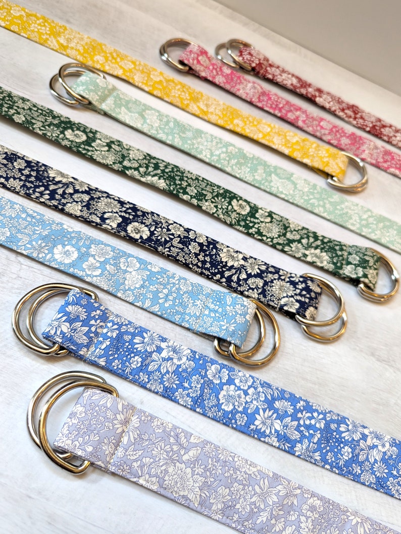 Puede incluir: Un conjunto de siete cinturones de tela coloridos con un patr&oacute;n floral. Cada cintur&oacute;n tiene una hebilla de doble D de plata.