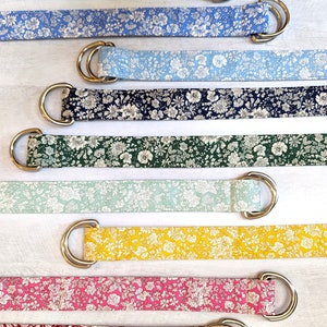 Puede incluir: Surtido de cinturones de tela coloridos con estampados florales y hebillas de argolla en D plateadas. Los cinturones est&aacute;n dispuestos en una pila vertical, con el color m&aacute;s claro en la parte superior y el color m&aacute;s oscuro en la parte inferior.