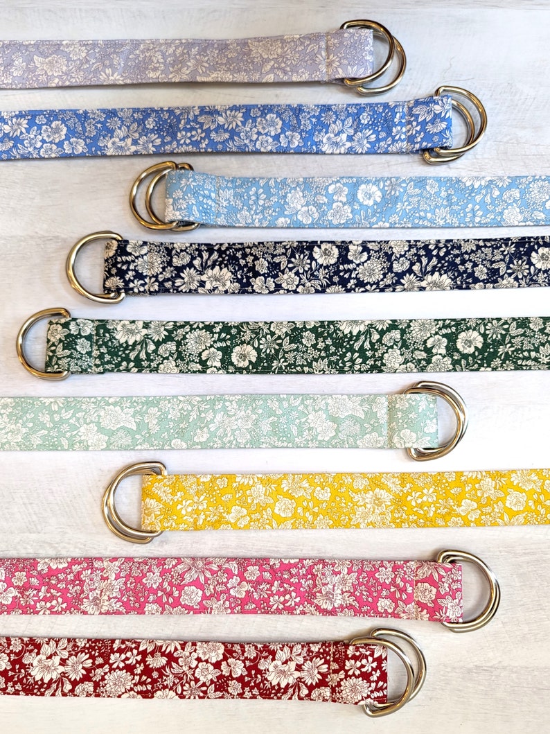 Puede incluir: Surtido de cinturones de tela coloridos con estampados florales y hebillas de argolla en D plateadas. Los cinturones est&aacute;n dispuestos en una pila vertical, con el color m&aacute;s claro en la parte superior y el color m&aacute;s oscuro en la parte inferior.