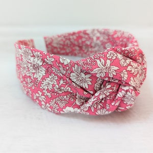 May include: A pink headband with a white floral pattern. The headband is knotted on top.