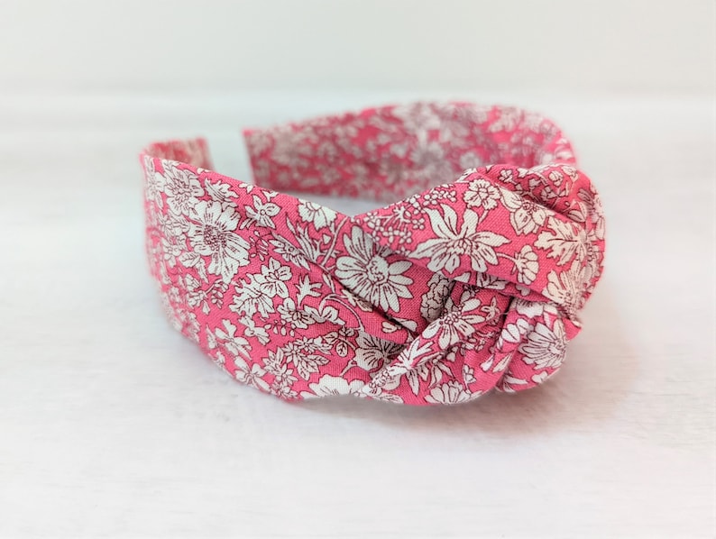 May include: A pink headband with a white floral pattern. The headband is knotted on top.
