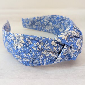 May include: A blue headband with a white floral pattern. The headband is knotted on top and has a stretchy elastic band.