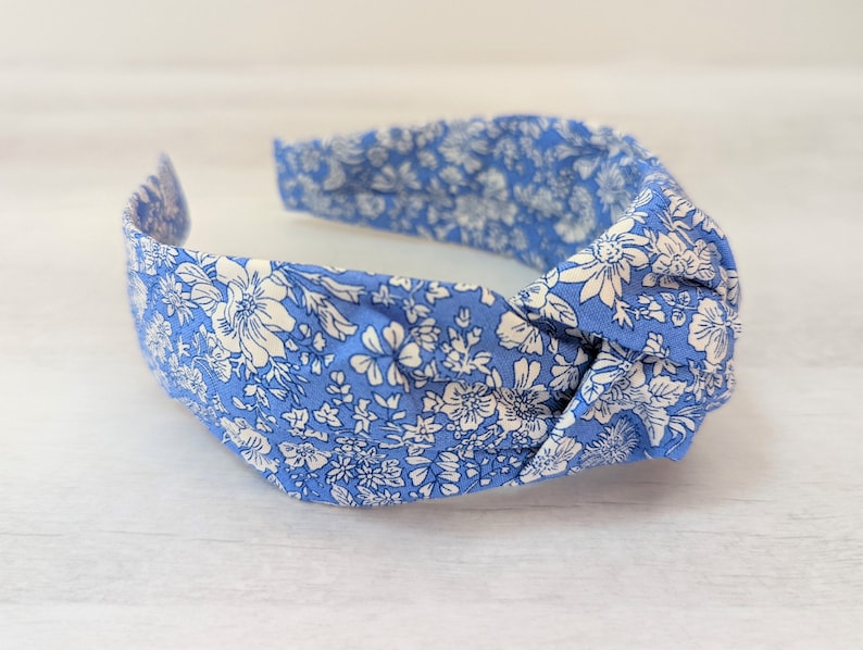 May include: A blue headband with a white floral pattern. The headband is knotted on top and has a stretchy elastic band.