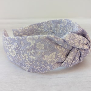 May include: A light purple fabric headband with a white floral pattern. The headband is knotted on top.