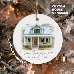 May include: A round white ceramic ornament featuring a watercolor illustration of a green house with a blue roof and a wooden door. The text reads CUSTOM HOUSE ORNAMENT, The Simpsons, 123 CANOPY STREET, 2025, and UNLIMITED PROOFS.