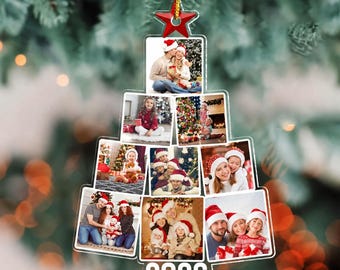 May include: A clear acrylic Christmas tree-shaped ornament featuring a collage of ten family photographs, a red star at the top, and the year 2026 printed in white at the base. The ornament hangs from a gold string against a blurred green background.