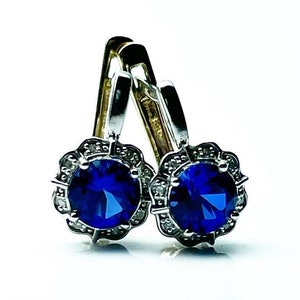 May include: A pair of silver earrings with blue gemstones surrounded by smaller clear gemstones.
