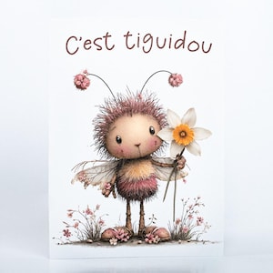 May include: A greeting card with a cartoon illustration of a fluffy, pinkish-brown creature holding a white and yellow daffodil. The card has the French text "C'est tiguidou" in brown script at the top, with a whimsical design.