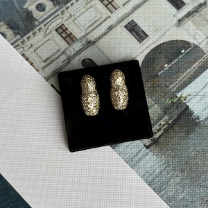 May include: A pair of gold glitter hoop earrings on a black velvet background.