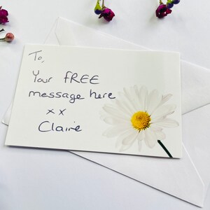 May include: A white card with a handwritten message that says "To, Your FREE message here xx Claire" and a white daisy with a yellow centre.
