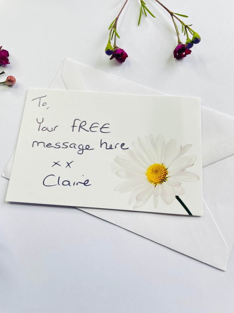 May include: A white card with a handwritten message that says "To, Your FREE message here xx Claire" and a white daisy with a yellow centre.