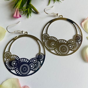 May include: A pair of silver hoop earrings with a delicate, circular design. The earrings feature a series of concentric circles, creating a geometric pattern.