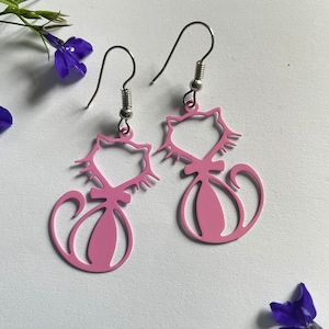 Può includere: Un paio di orecchini a forma di gatto rosa con ganci d'argento. I gatti sono contornati d'argento e hanno un design delicato e fantasioso.