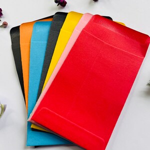 May include: A set of six colourful envelopes in black, orange, blue, yellow, pink, and red. The envelopes are made of a smooth, textured paper and are ideal for sending cards, letters, or small gifts.