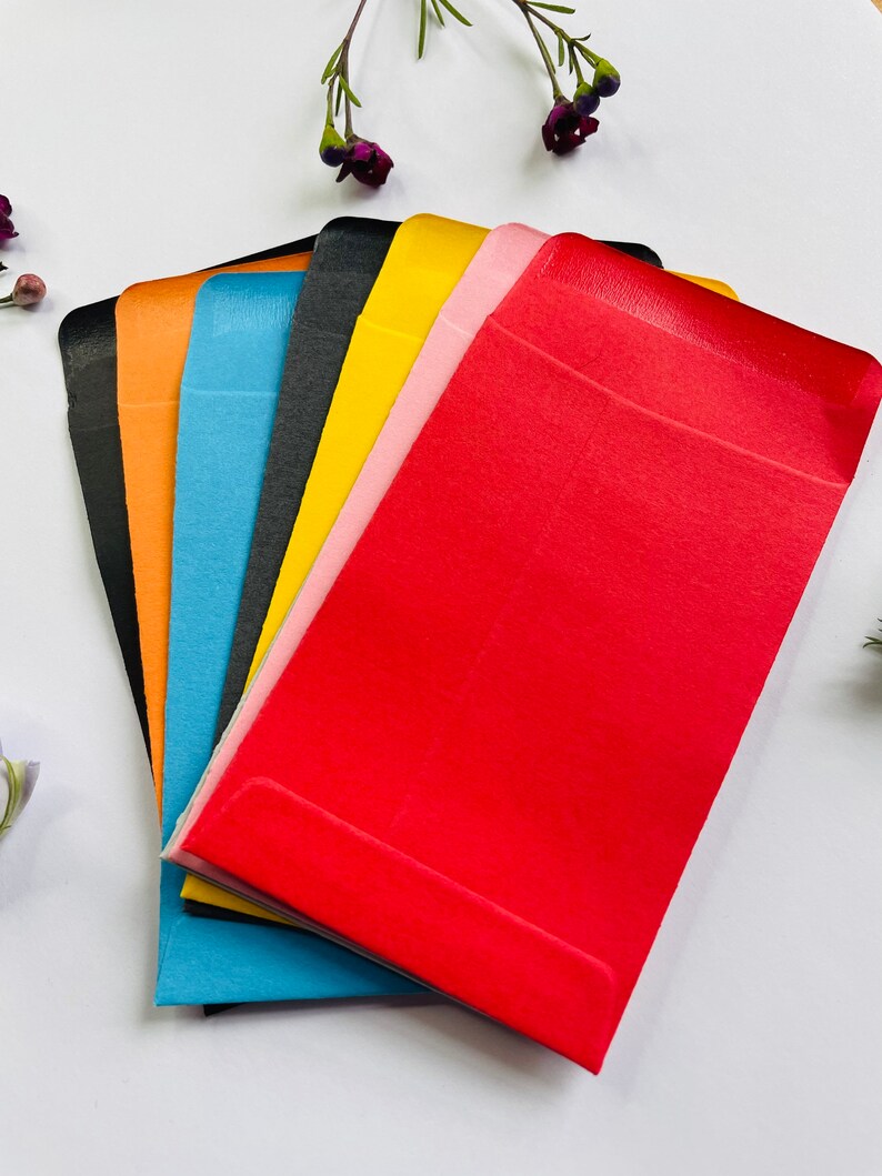 May include: A set of six colourful envelopes in black, orange, blue, yellow, pink, and red. The envelopes are made of a smooth, textured paper and are ideal for sending cards, letters, or small gifts.