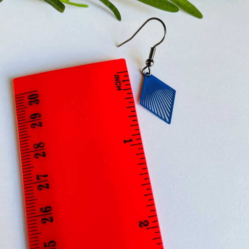 May include: A pair of blue diamond-shaped earrings with a linear design. The earrings are approximately 2.5 cm in length.