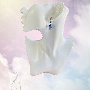 May include: A pair of blue diamond-shaped earrings with silver hooks. The earrings are on a white mannequin head against a cloudy background.