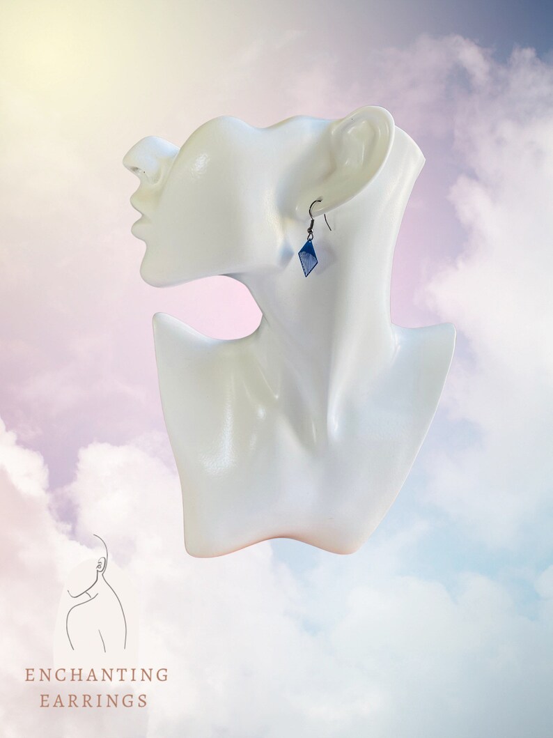 May include: A pair of blue diamond-shaped earrings with silver hooks. The earrings are on a white mannequin head against a cloudy background.