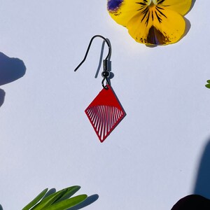 May include: Red diamond-shaped earrings with a geometric design. The earrings have a silver hook.