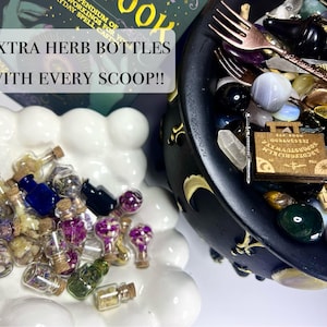 May include: A collection of small glass herb bottles with cork stoppers, in various colors, sits on a white, cloud-shaped dish. A black cauldron filled with crystals, a wooden planchette, and a fork is also visible. Text reads: "EXTRA HERB BOTTLES WITH EVERY SCOOP!!"