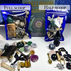 May include: Two blue bags labeled "Full Scoop" and "Half Scoop" filled with assorted crystals, charms, and small objects. A book titled "Spell Book" is visible in the background. Various crystals and charms are scattered in front of the bags.