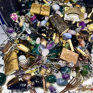 May include: A collection of various decorative items, including gemstones, charms, and small trinkets, spilling from a black bucket. The items are in various colors, including green, purple, and gold. Some items have text, including an Ouija board.