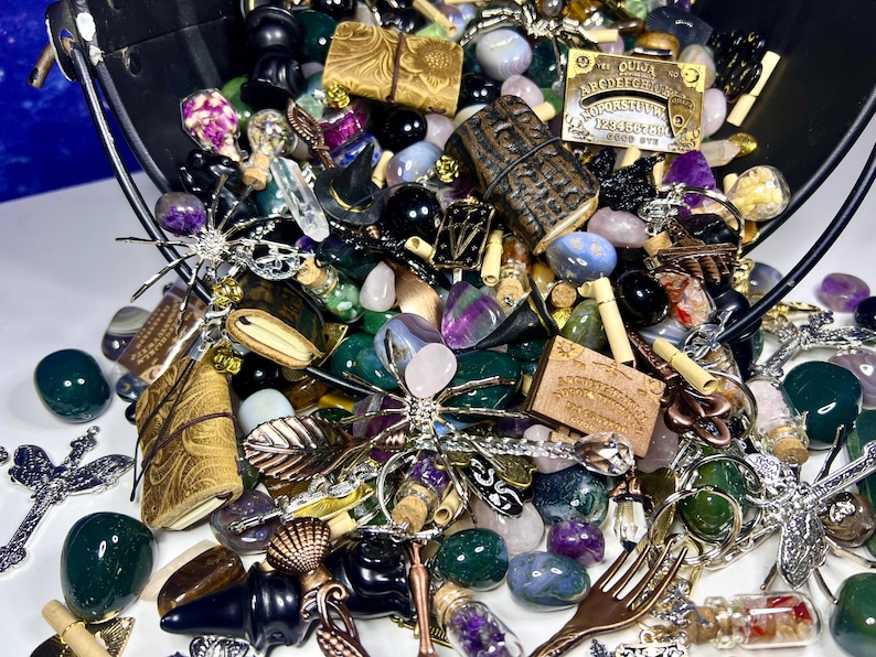May include: A collection of various decorative items, including gemstones, charms, and small trinkets, spilling from a black bucket. The items are in various colors, including green, purple, and gold. Some items have text, including an Ouija board.