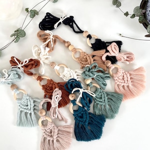 May include: Assortment of handmade macrame tassel keychains with wooden rings. The tassels are in various colours, including teal, pink, brown, and white.