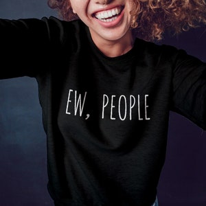 May include: Black sweatshirt with the text "EW, PEOPLE" in white. The sweatshirt is a long-sleeved crew neck. The image shows a person wearing the sweatshirt, smiling.