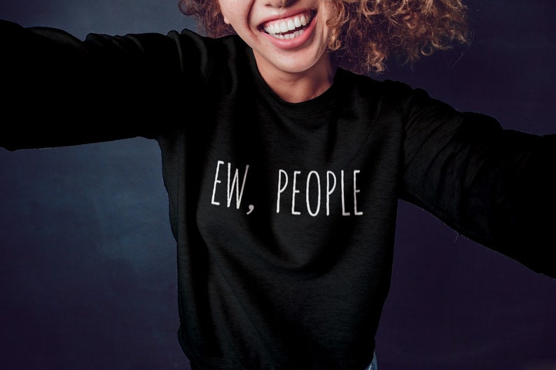 May include: Black sweatshirt with the text "EW, PEOPLE" in white. The sweatshirt is a long-sleeved crew neck. The image shows a person wearing the sweatshirt, smiling.