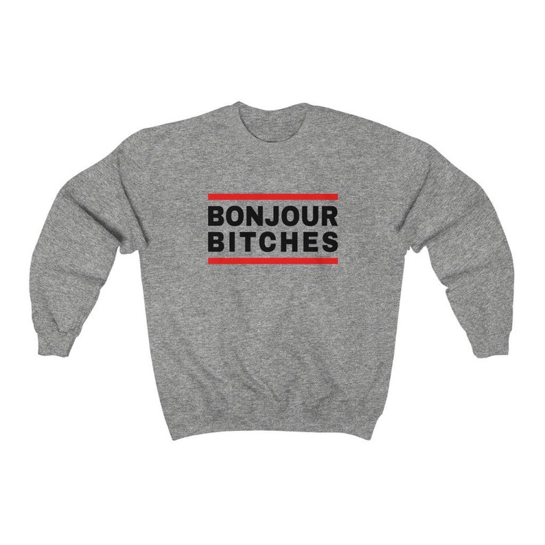 May include: A heather gray sweatshirt with the phrase "BONJOUR BITCHES" in black block letters, framed by two red horizontal lines. The sweatshirt has long sleeves and a crew neck.
