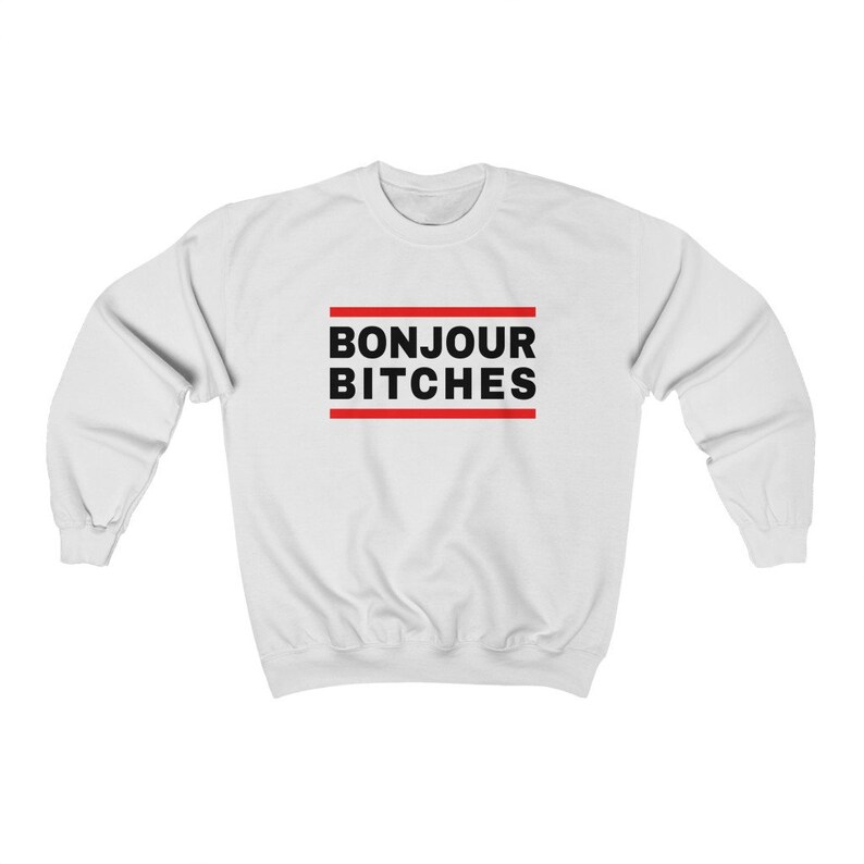 May include: White sweatshirt with the text "BONJOUR BITCHES" in black, framed by two red horizontal lines. The sweatshirt is a casual, long-sleeved garment.