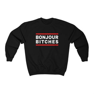 May include: Black sweatshirt with the text "BONJOUR BITCHES" in white, framed by two red lines. The sweatshirt is a crew neck style, suitable for casual wear.
