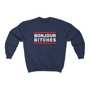 May include: Navy blue sweatshirt with the text "BONJOUR BITCHES" in white, framed by two red lines. The sweatshirt is a casual garment, suitable for everyday wear.