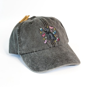 May include: A black baseball cap with a black cat surrounded by colourful butterflies embroidered on the front.