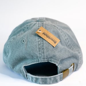May include: A green, cotton baseball cap with an adjustable strap and a brown tag that reads "Beechfield Original Headwear".