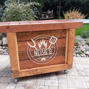 May include: A wooden mobile barbecue cart with wheels. The cart has a wooden top and a logo that says "Nebie's Barbecue" with a flame and grilling tools.