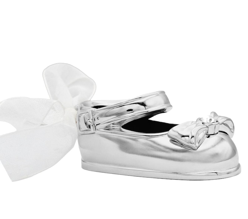 May include: A silver baby shoe with a white satin bow. The shoe is a decorative keepsake for a new baby.