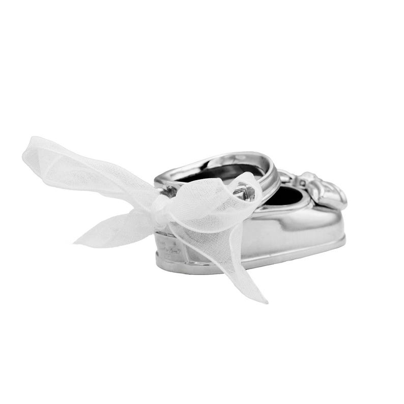 May include: Silver baby shoe ring holder with a white satin ribbon bow. The shoe is open at the top and has a small ring inside.
